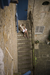 Italien, Toskana, Frau sitzt auf der Treppe eines Landhauses und zeichnet ein Bild - RIBF000389