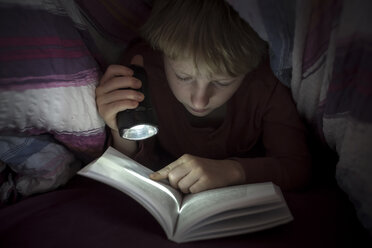 Junge mit Taschenlampe, der unter einer Decke ein Buch liest - SARF002304