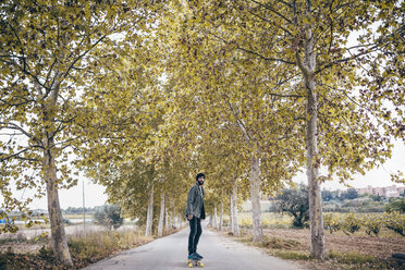 Spain, Tarragona, young man with longboard on autumnal country road - JRFF000174