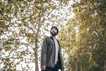 Spain, Tarragona, portrait of bearded young man standing in front of autumnal trees - JRFF000175