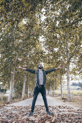 Spain, Tarragona, young man standing on country road throwing autumn leaves in the air - JRFF000181