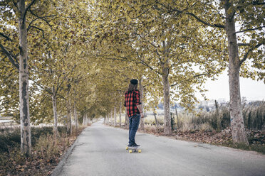 Spain, Tarragona, back view of man with longboard on autumnal country road - JRFF000194