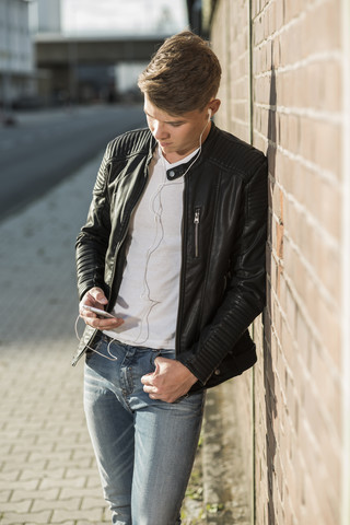 Junger Mann mit Ohrstöpseln, der auf sein Mobiltelefon schaut, lizenzfreies Stockfoto