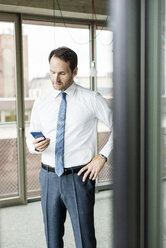 Porträt eines Geschäftsmannes, der auf sein Smartphone schaut - UUF005971