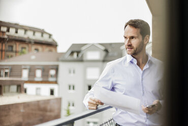 Portrait of businessman with sheet of paper and smartphone looking at distance - UUF006013