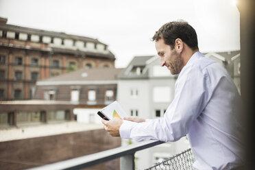 Lächelnder Geschäftsmann schaut auf sein Smartphone - UUF006014