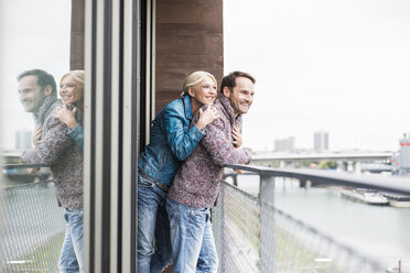 Glückliches Paar steht zusammen auf einem Balkon und schaut in die Ferne - UUF006019