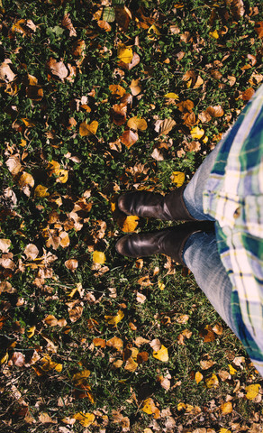 Teilansicht einer Frau, die auf einer mit Herbstblättern bedeckten Wiese steht, lizenzfreies Stockfoto