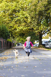 Deutschland, Kiel, kleines Mädchen läuft mit ihrem Mischlingshund auf dem Bürgersteig - JFEF000743