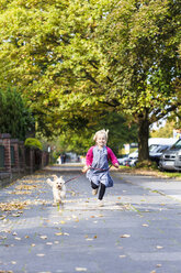 Germany, Kiel, little girl running with her mongrel on pavement - JFEF000743