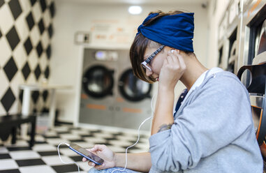 Junge Frau hört Musik mit Kopfhörern in einem Waschsalon - MGOF001028