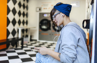 Junge Frau hört Musik mit Kopfhörern in einem Waschsalon - MGOF001029