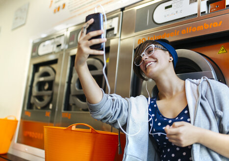 Junge Frau macht ein Selfie mit Smartphone in einem Waschsalon - MGOF001030