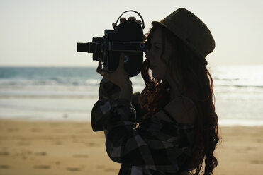 Spain, El Puerto de Santa Maria, silhouette of young woman using old film camera on the beach - KIJF000025