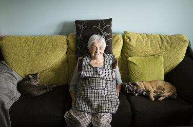 Porträt einer älteren Frau, die mit ihren beiden schlafenden Katzen zu Hause auf der Couch sitzt - RAEF000655