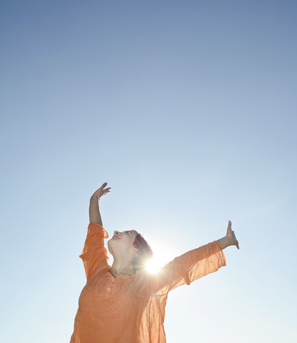 Glückliche junge Frau gegen die Sonne, blauer Himmel, lizenzfreies Stockfoto