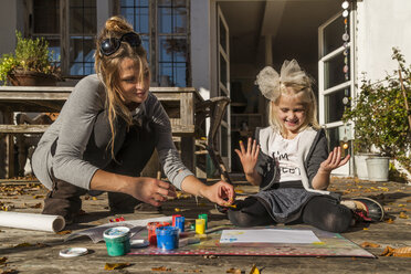 Mutter und ihre kleine Tochter malen mit Fingerfarben auf der Terrasse - TCF004920