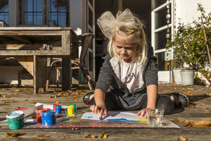 Blondes kleines Mädchen malt mit Fingerfarben auf der Terrasse - TCF004921