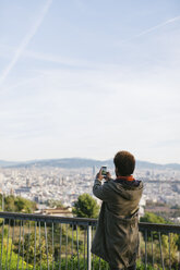 Spain, Barcelona, back view of young man taking a picture of view with his smartphone - EBSF001043