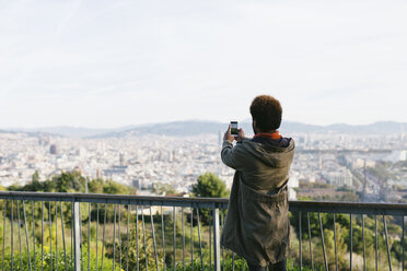 Spain, Barcelona, back view of young man taking a picture of view with his smartphone - EBSF001044