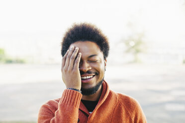 Portrait of smiling young man with closed eyes and hand on his face - EBSF001059