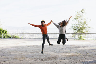 Spain, Barcelona, portrait of happy young couple jumping in the air on view terrace - EBSF001066