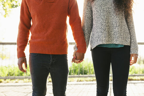 Young couple wearing knit pullovers standing side by side holding hands, partial view - EBSF001069