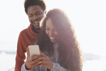 Porträt eines glücklichen jungen Paares mit Smartphone im Gegenlicht - EBSF001072