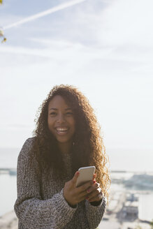 Spanien, Barcelona, Porträt einer lächelnden jungen Frau mit Smartphone im Gegenlicht - EBSF001075