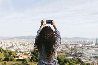 Spanien, Barcelona, Rückenansicht einer jungen Frau, die mit ihrem Smartphone ein Foto von der Aussicht macht - EBSF001077