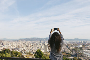 Spain, Barcelona, back view of young woman taking a picture of view with her smartphone - EBSF001078