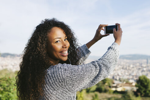 Spanien, Barcelona, Porträt einer jungen Frau, die mit ihrem Smartphone eine Aussicht fotografiert - EBSF001079