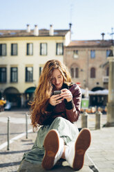 Italien, Padua, Frau sitzt im Freien auf dem Stadtplatz mit Mobiltelefon - GIOF000488