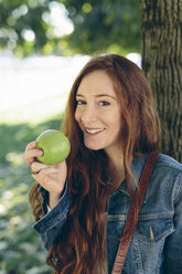 Lächelnde Frau hält einen Apfel im Park - GIOF000499