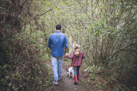 Rückenansicht von Vater und kleiner Tochter, die mit ihrer französischen Bulldogge im Wald spazieren gehen, lizenzfreies Stockfoto