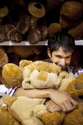 Lächelnder Mann, der Teddybären in einem Geschäft umarmt - RMAF000241