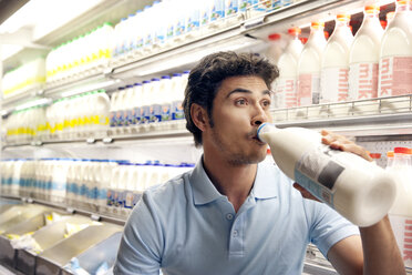 Mann trinkt Milch vor einem Kühlschrank in einem Supermarkt - RMAF000245