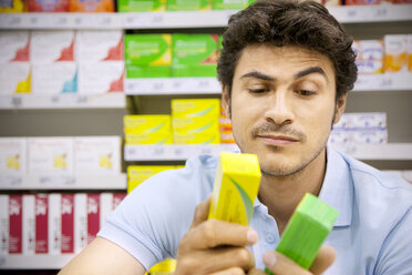 Porträt eines Mannes in einem Supermarkt, der zwei Produkte vergleicht - RMAF000248