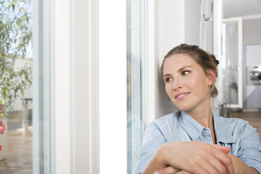 Young woman sitting at the window, hugging knees - FKF001546