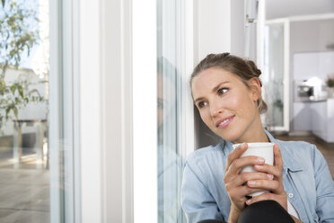 Young woman sitting at the window, drinking coffee - FKF001547