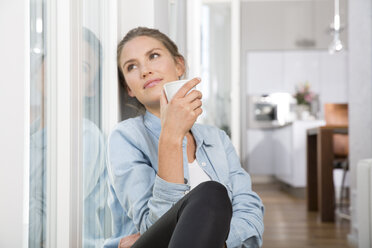 Junge Frau sitzt am Fenster und trinkt Kaffee - FKF001552