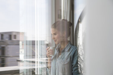 Young woman standing at the window, drinking coffee - FKF001553