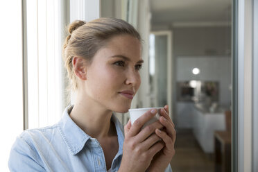 Young woman standing at the window, drinking coffee - FKF001558