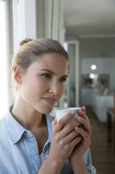 Junge Frau steht am Fenster und trinkt Kaffee - FKF001559