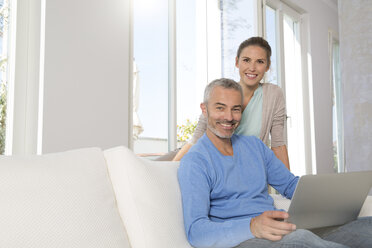 Couple relaxing on couch at home using laptop - FKF001567