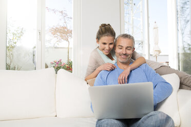 Ehepaar entspannt sich auf der Couch zu Hause und benutzt einen Laptop - FKF001575