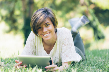 Portrait of smiling teenage girl lying in grass with digital tablet - GIOF000518