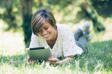 Teenage girl lying in grass looking at digital tablet - GIOF000519