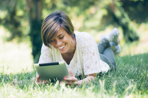 Teenager-Mädchen liegt im Gras und schaut auf ein digitales Tablet - GIOF000519
