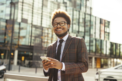 Lächelnder junger Geschäftsmann im Freien mit Mobiltelefon, lizenzfreies Stockfoto